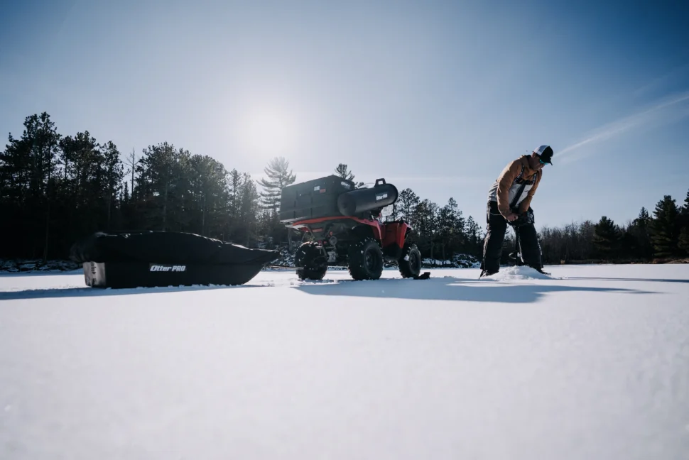 Ice angler drilling a hole beside an ATV during first ice.