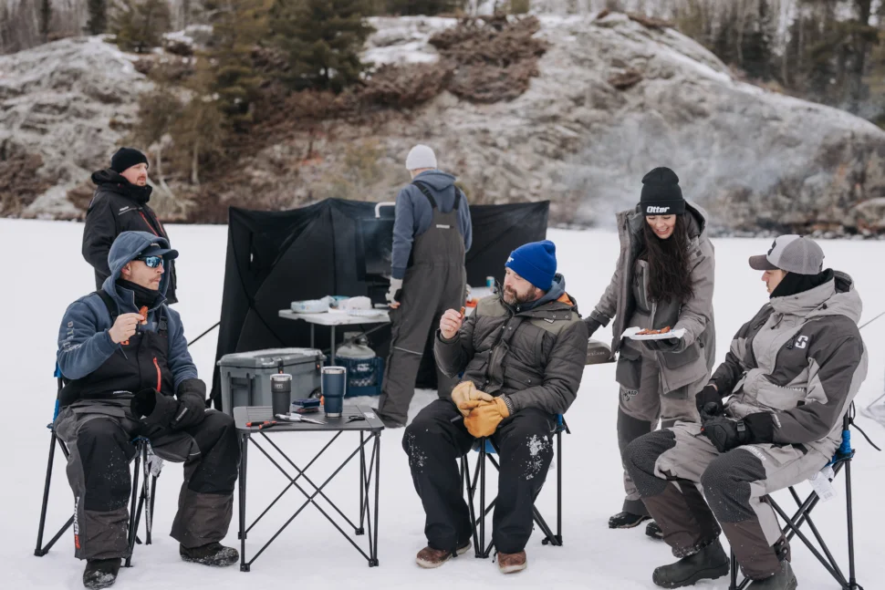 Friends cooking breakfast and spending time together while ice fishing.