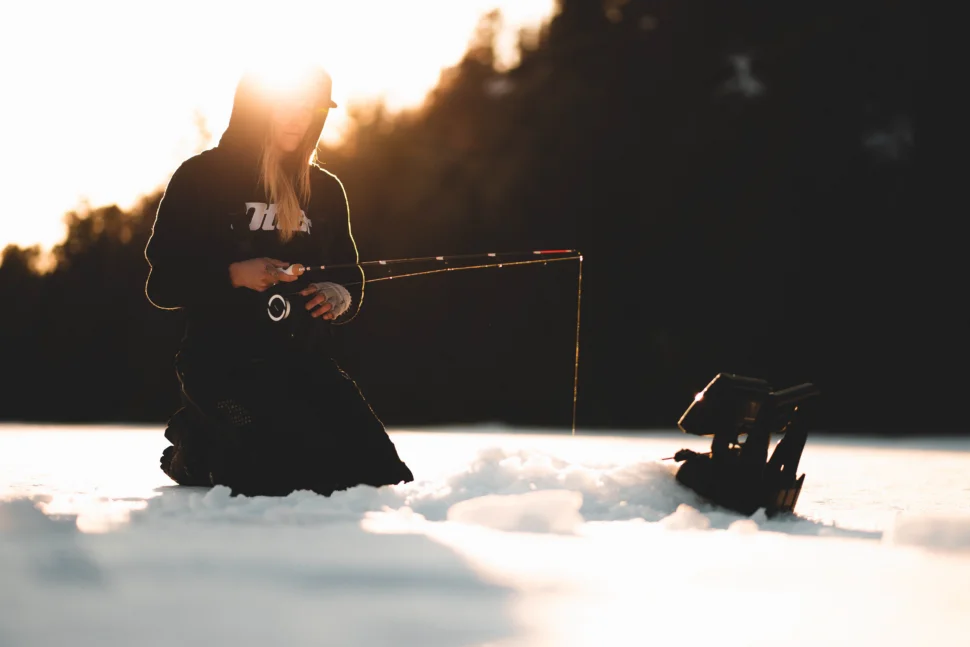 Ice angler fishing on a frozen lake during sunrise.